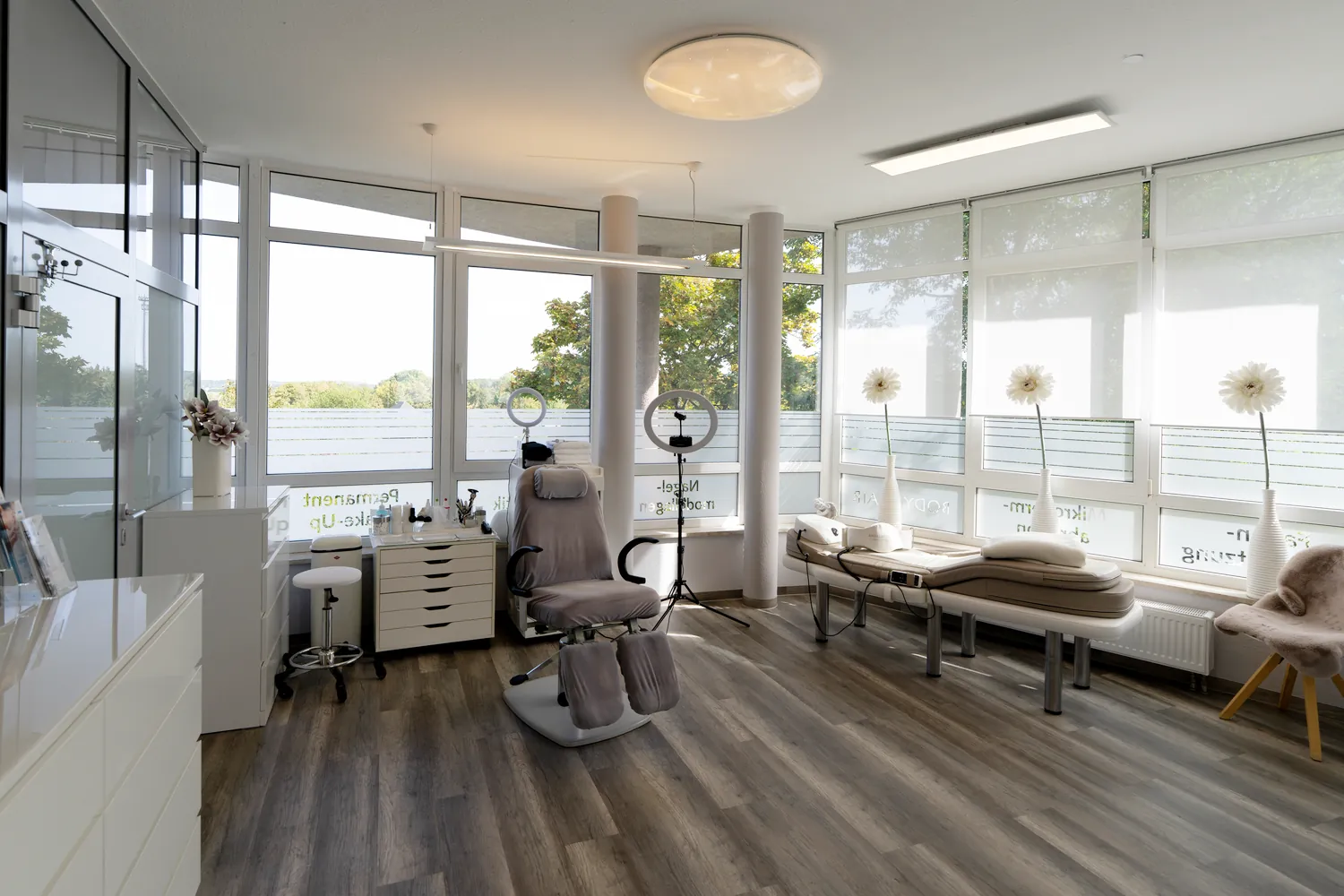 Heller Behandlungsraum mit Behandlungsstuhl, Liege und großer Fensterfront bei BodyFlair Werdau